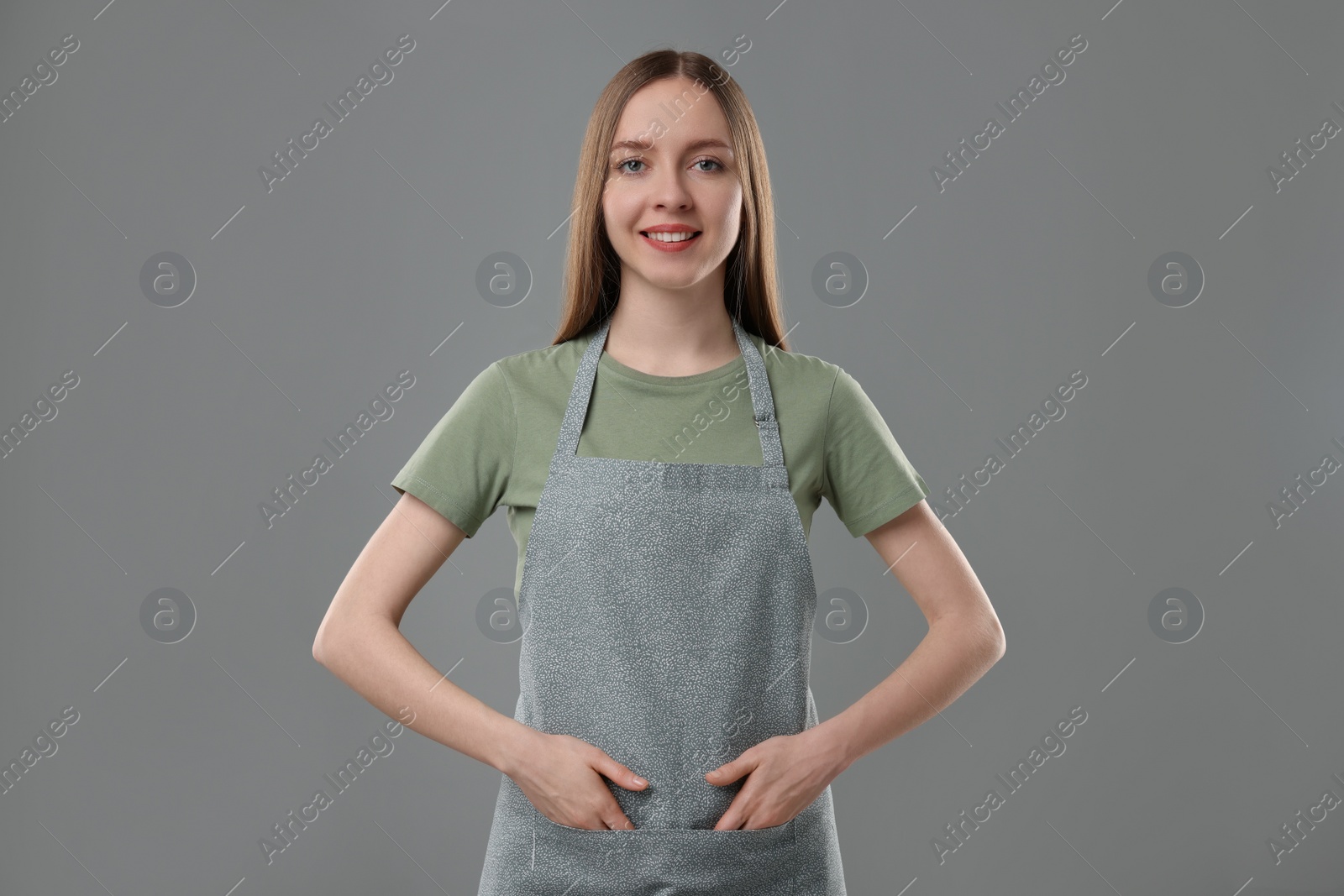 Photo of Beautiful young woman wearing kitchen apron on grey background. Mockup for design