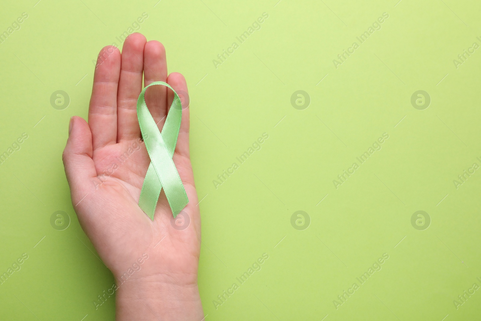 Photo of World Mental Health Day. Woman holding green ribbon on color background, top view with space for text