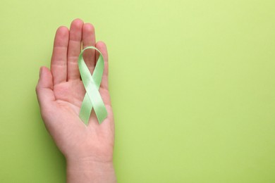 World Mental Health Day. Woman holding green ribbon on color background, top view with space for text
