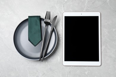 Photo of Business lunch concept. Plate, cutlery, tie and tablet with space for text on light gray marble table, flat lay
