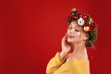 Beautiful young woman wearing Christmas wreath on red background. Space for text