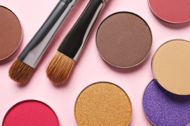 Different beautiful eye shadows and makeup brushes on pink background, flat lay