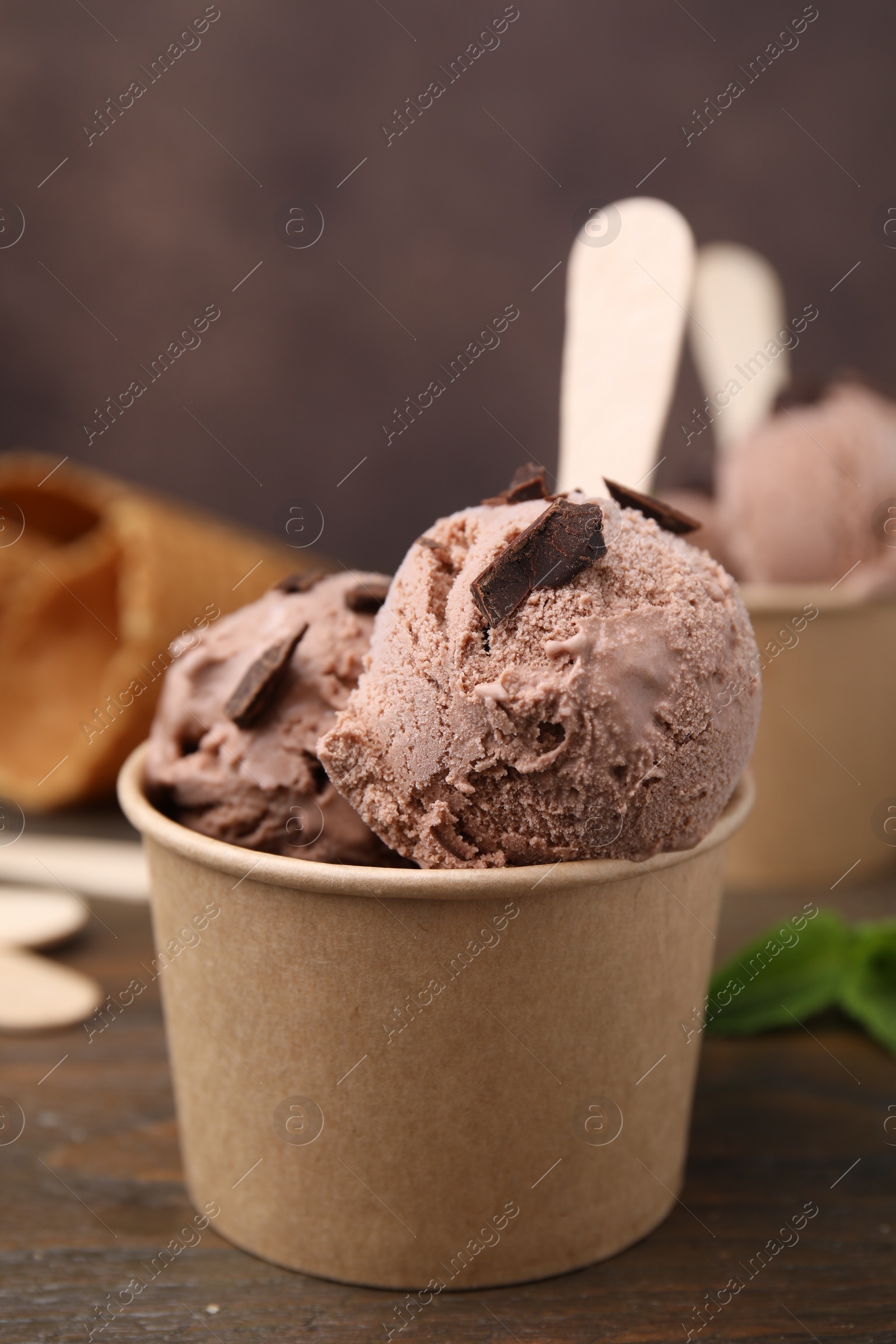 Photo of Paper cups with tasty chocolate ice cream on wooden table, closeup