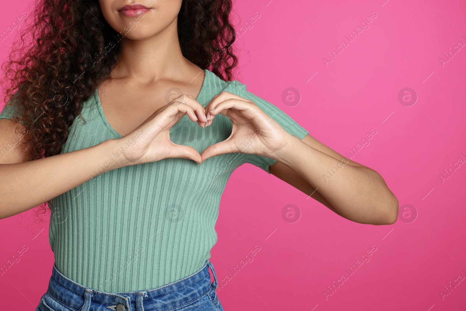 Photo of African-American woman making heart with hands on pink background, closeup