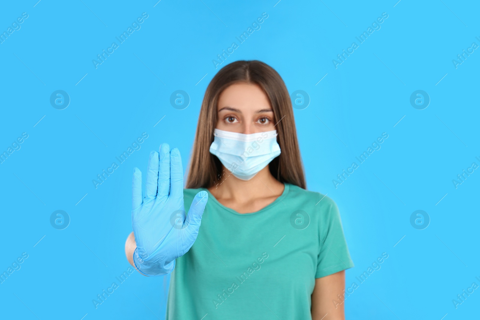 Photo of Woman in protective mask showing stop gesture on light blue background. Prevent spreading of COVID‑19