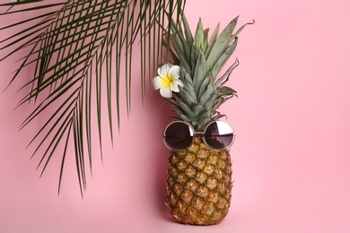 Pineapple with sunglasses, plumeria flower and palm tree leaves on pink background. Creative concept