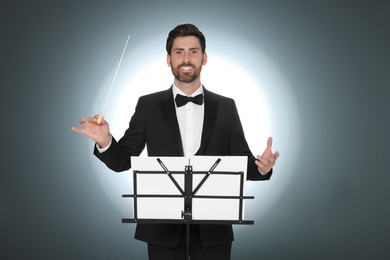 Happy professional conductor with baton and note stand on grey background