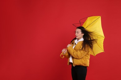 Photo of Woman with umbrella caught in gust of wind on red background. Space for text
