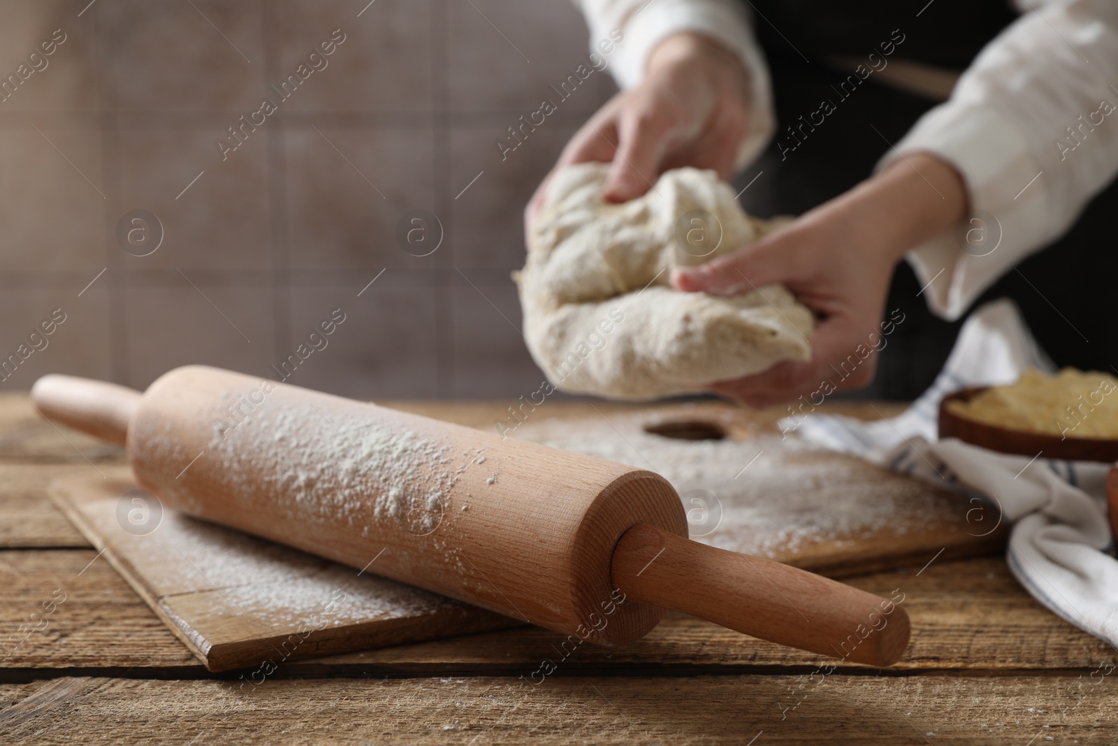 Photo of Woman making dough at wooden table, selective focus
