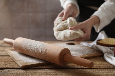 Photo of Woman making dough at wooden table, selective focus