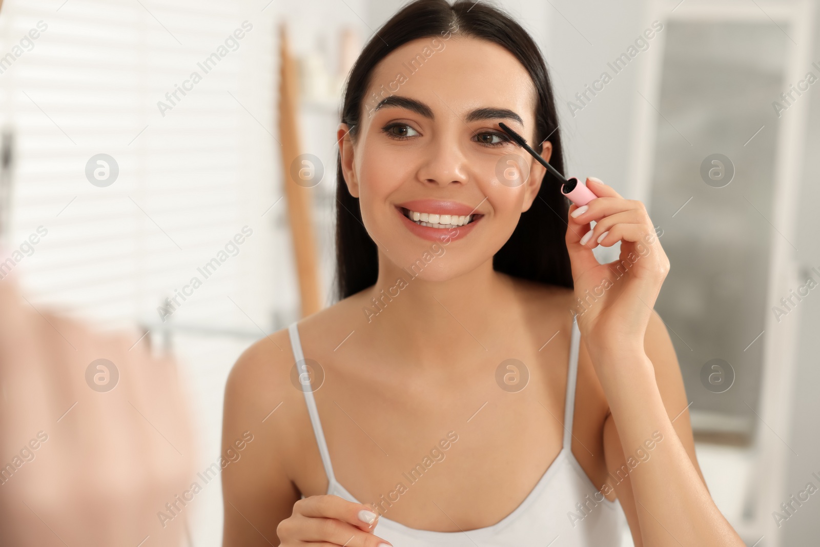 Photo of Beautiful young woman applying mascara near mirror in bathroom