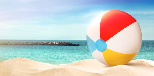 Image of Colorful beach ball on sandy coast near sea, space for text. Banner design 