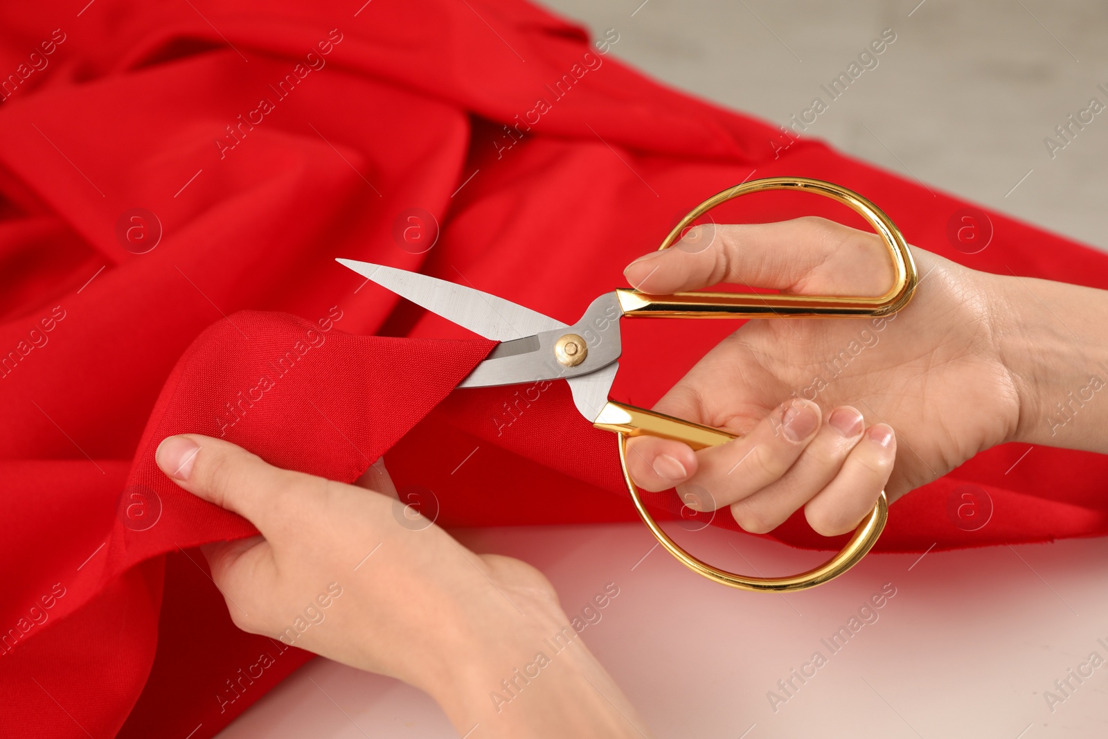 Photo of Woman cutting fabric with sharp scissors at white table, closeup