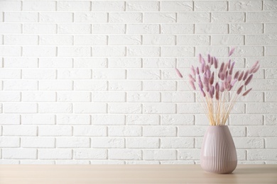 Photo of Dried flowers in vase on table against white brick wall. Space for text