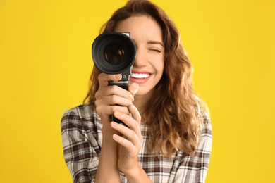 Beautiful young woman with vintage video camera against yellow background, focus on lens