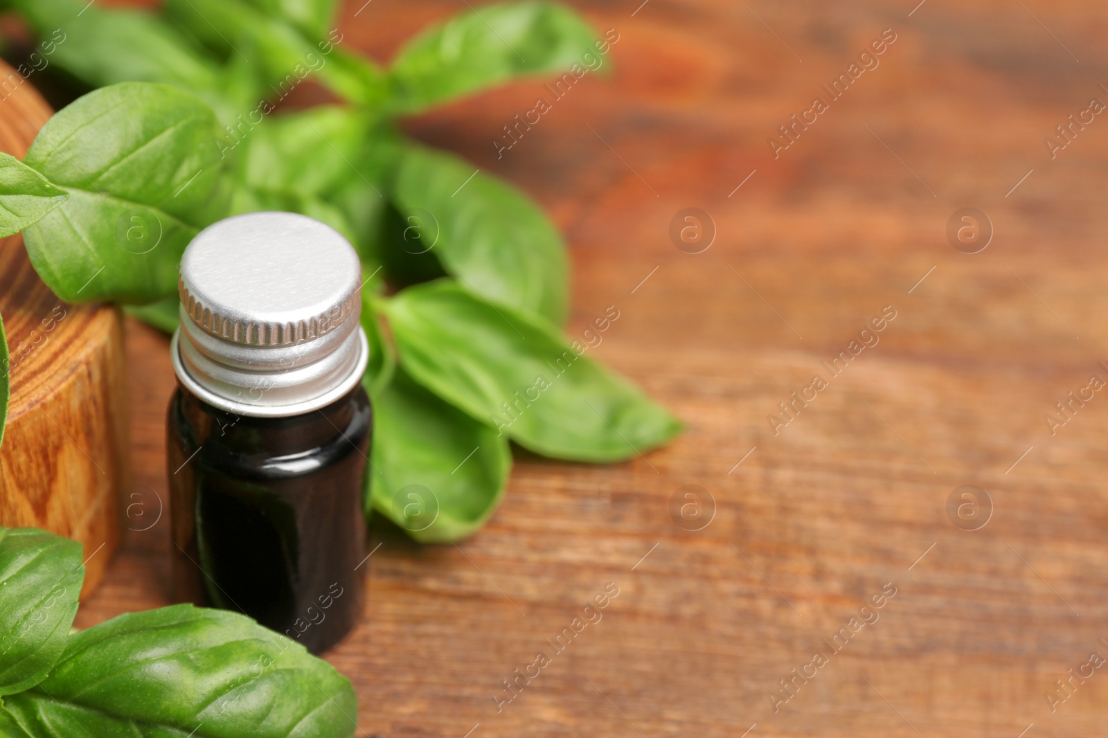 Photo of Glass bottle of basil oil with leaves and space for text on wooden table