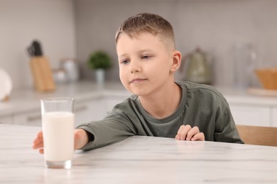 Photo of Cute boy reaching out for glass of milk at white table in kitchen