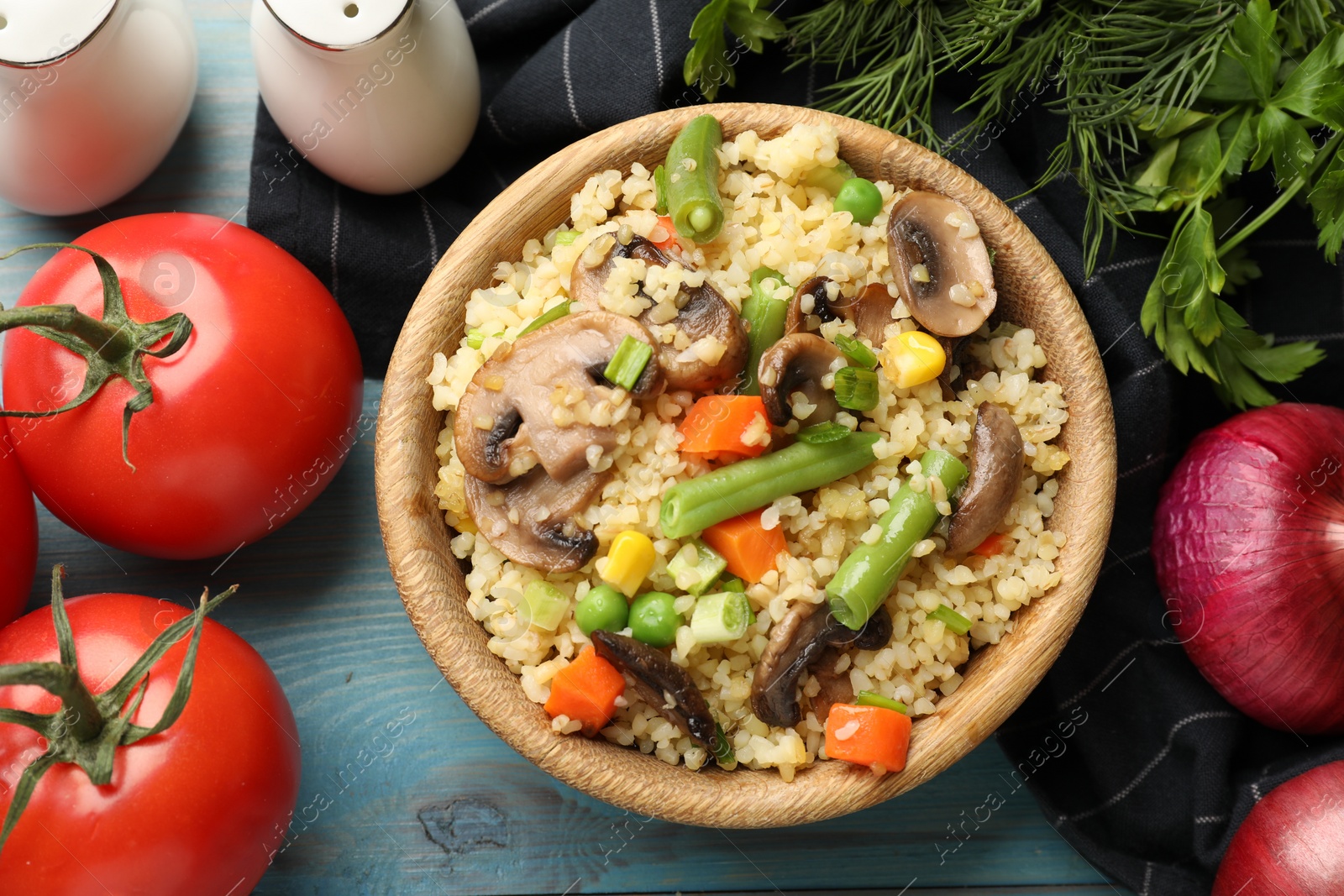 Photo of Delicious bulgur with vegetables, mushrooms and other products on light blue wooden table, flat lay