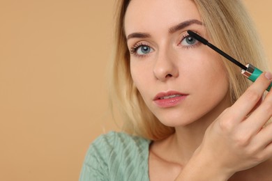 Photo of Beautiful woman applying mascara on beige background, closeup. Space for text