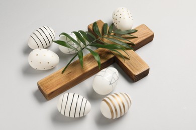 Wooden cross, painted Easter eggs and palm leaf on light grey background