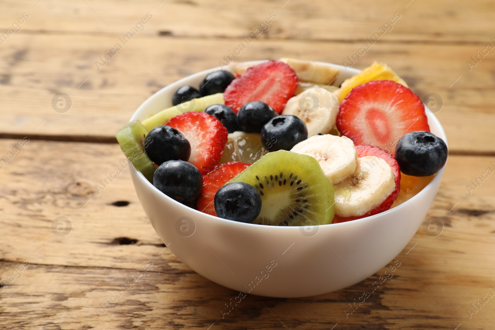 Photo of Tasty fruit salad in bowl on wooden table, closeup