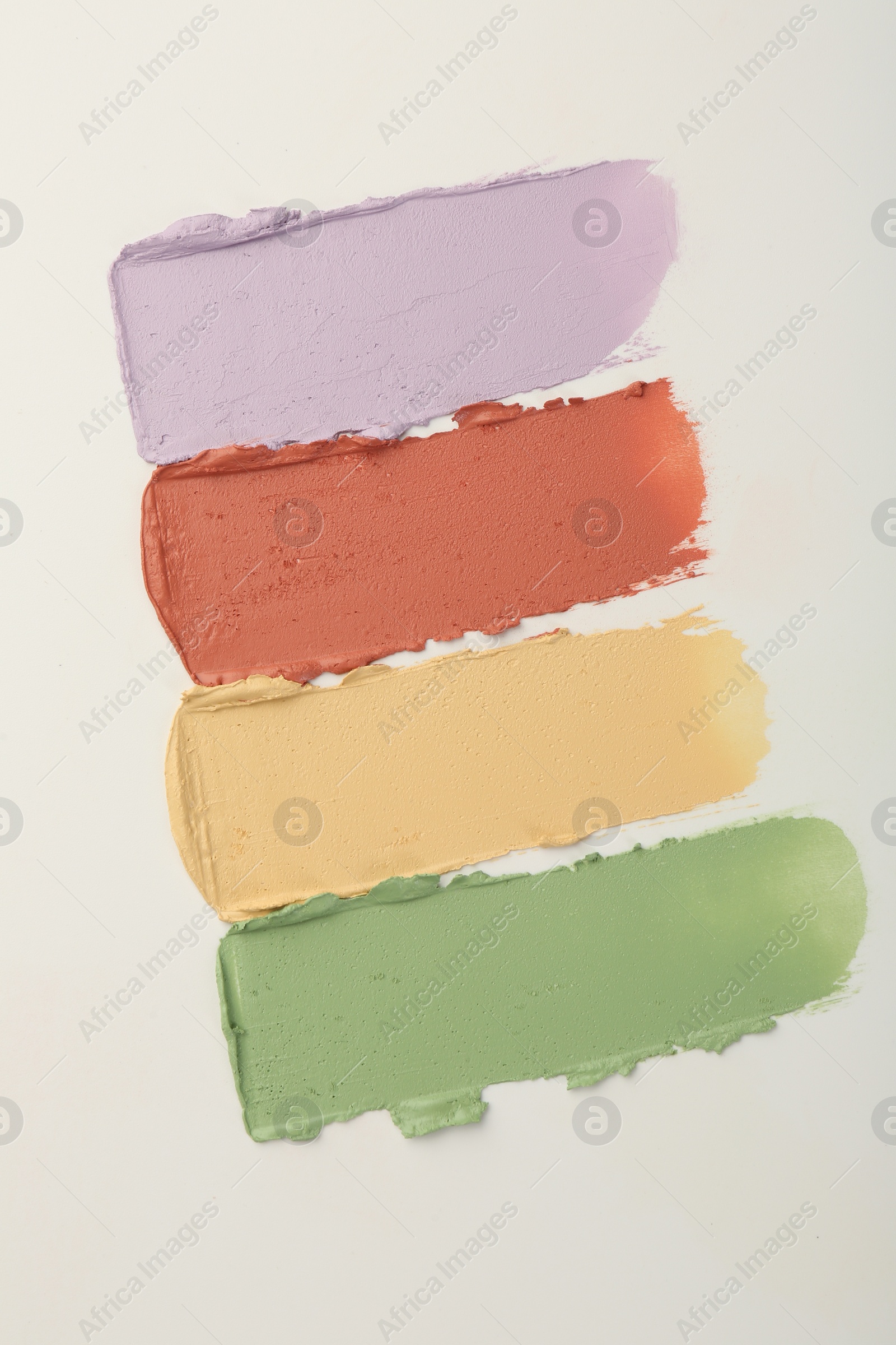 Photo of Samples of different color correcting concealers on white background, top view