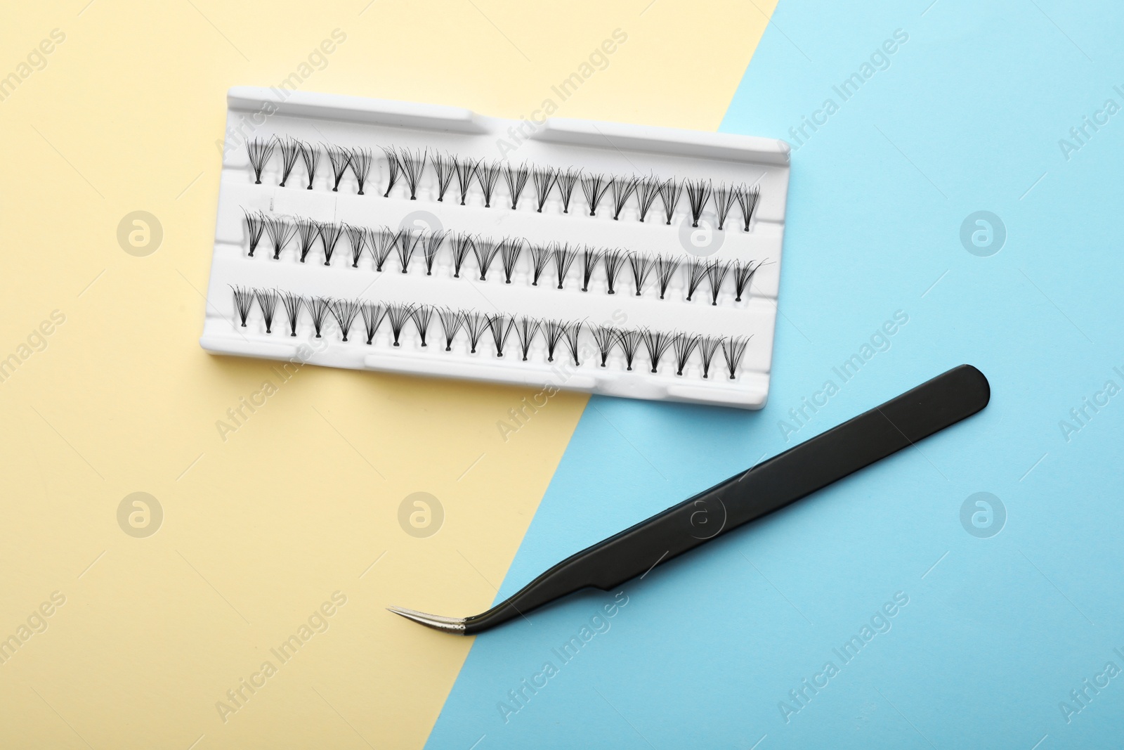 Photo of Artificial eyelashes and tweezers on color background, top view