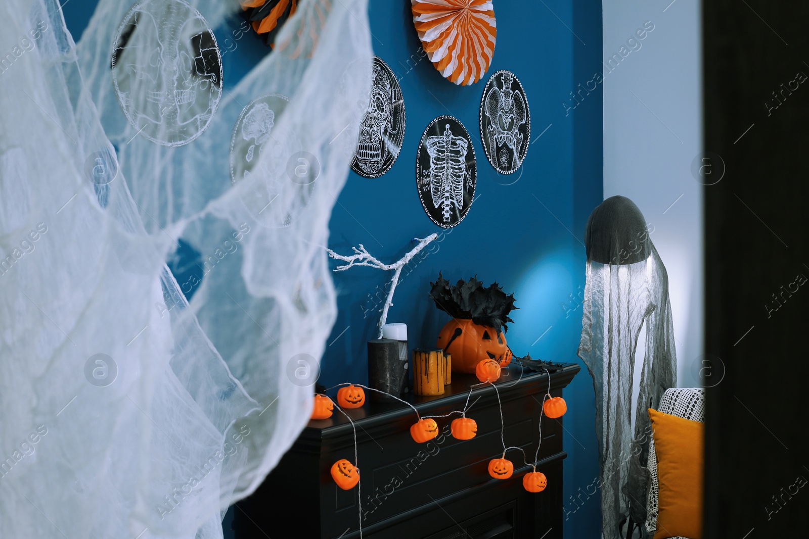 Photo of Jack-o'-lantern lights and different Halloween decorations on black fireplace near blue wall