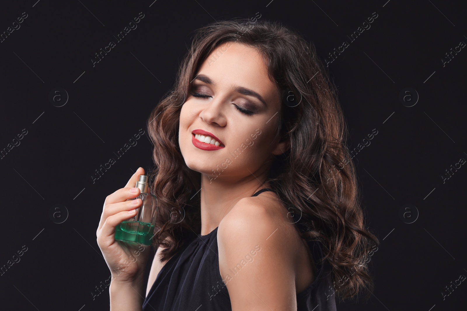 Photo of Beautiful young woman with bottle of perfume on black background