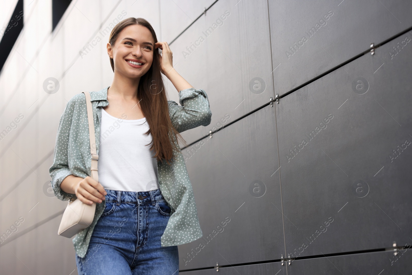 Photo of Young woman in casual clothes walking near grey wall outdoors, space for text