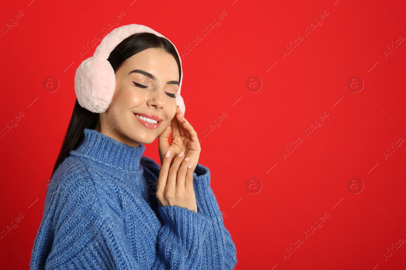 Photo of Beautiful young woman wearing earmuffs on red background. Space for text