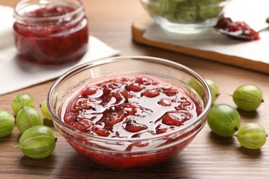 Photo of Bowl of delicious gooseberry jam and fresh berries on wooden table, closeup