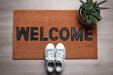 Photo of New clean mat with word WELCOME, shoes and plant on floor, top view
