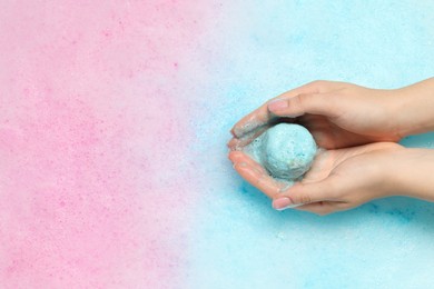 Photo of Woman holding bath bomb in water with foam, top view. Space for text