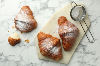 Photo of Tasty croissants with powdered sugar on white marble table, flat lay