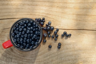 Photo of Cup of fresh bilberries on wooden table, top view. Space for text