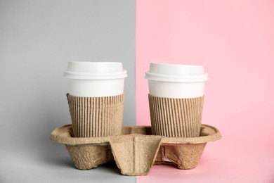 Takeaway paper coffee cups with sleeves and plastic lids in cardboard holder on color background