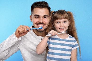 Photo of Little girl and her father brushing teeth together on color background