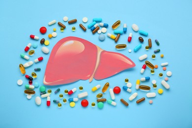 Paper liver and pills on light blue background, flat lay. Hepatitis treatment