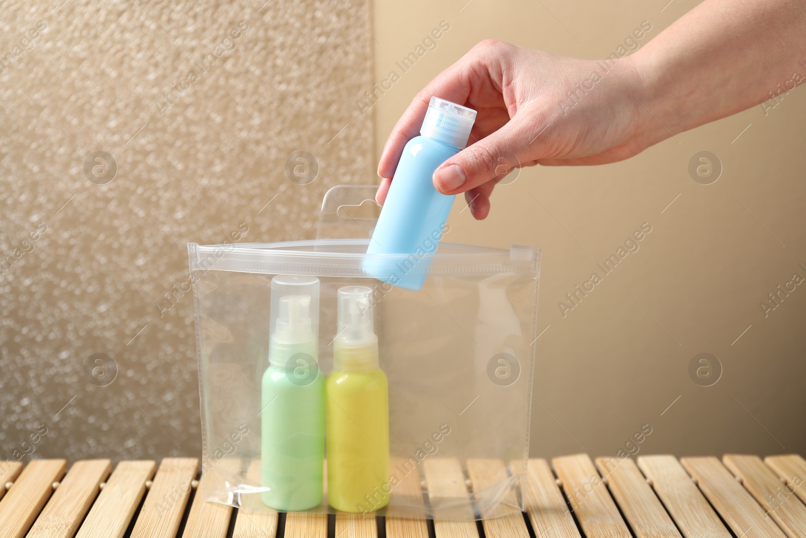 Photo of Woman packing cosmetic travel kit at wooden table, closeup. Bath accessories