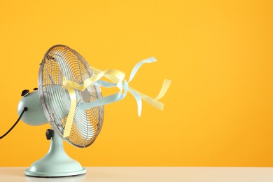 Photo of Electric fan on white table against yellow background, space for text. Summer heat