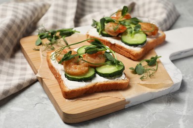 Photo of Tasty toasts with cream cheese, shrimps, cucumbers and microgreens served on grey marble table, closeup