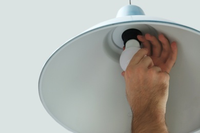 Photo of Man changing light bulb in lamp on white background, closeup