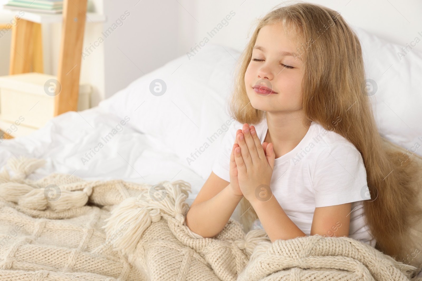 Photo of Girl with clasped hands praying on bed at home, space for text