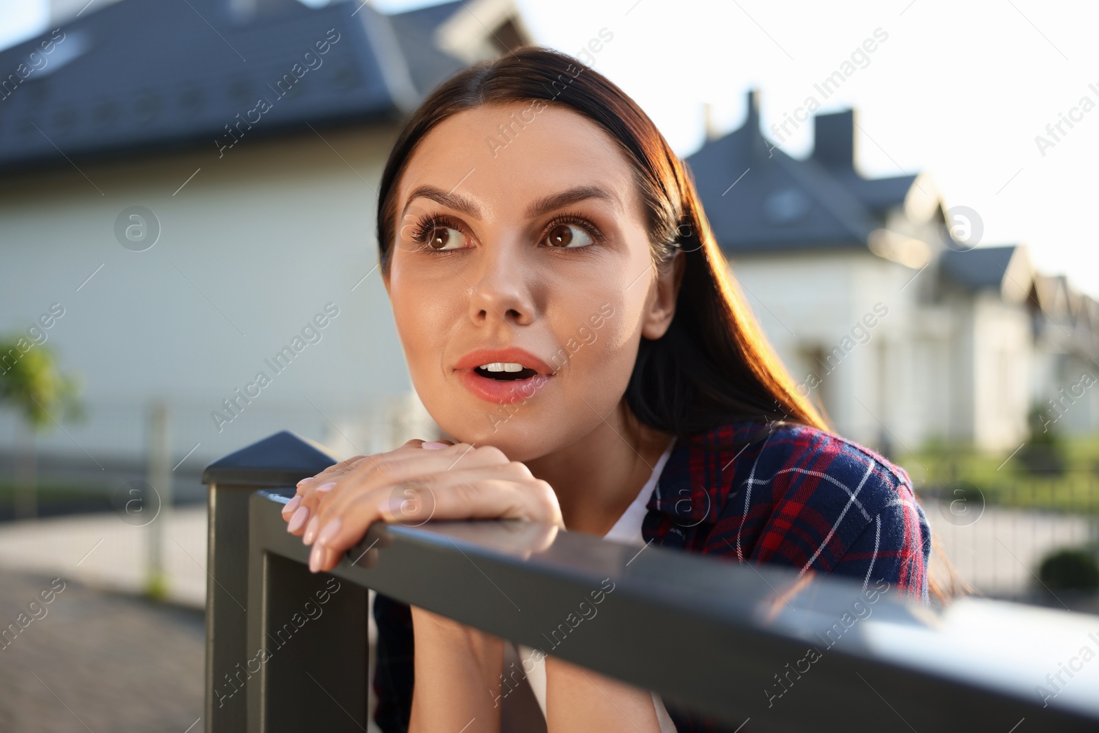 Photo of Concept of private life. Curious young woman spying on neighbours over fence outdoors