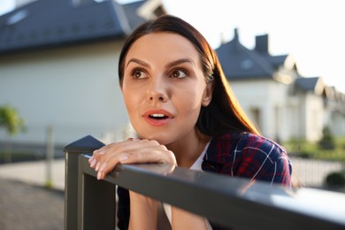 Photo of Concept of private life. Curious young woman spying on neighbours over fence outdoors