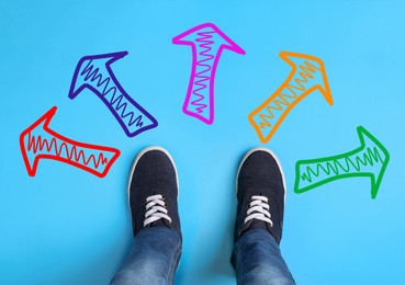Image of Choosing future profession. Teenager standing in front of drawn signs on light blue background, top view. Arrows pointing in different directions symbolizing diversity of opportunities