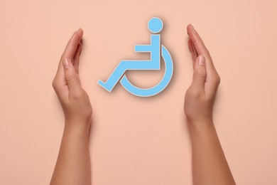 Image of Disability inclusion. Woman protecting wheelchair symbol on pale pink background, closeup