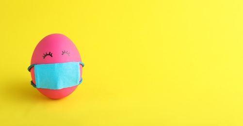 Photo of Bright egg in protective mask on yellow background, space for text. Easter holiday during coronavirus quarantine