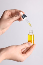 Photo of Woman holding bottle of cosmetic oil on light background, closeup